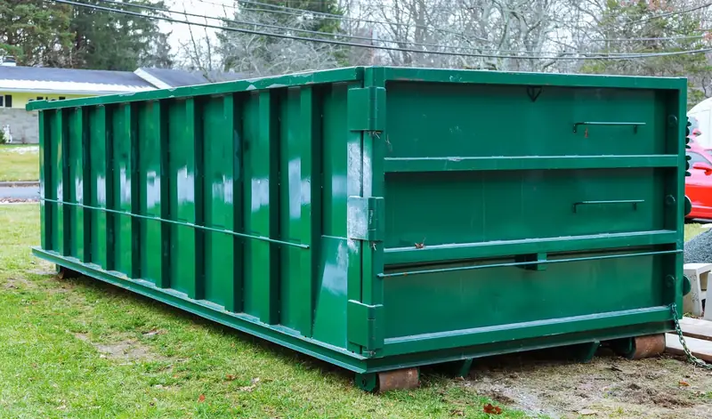 Green roll-off dumpster set on wooden boards beside a home